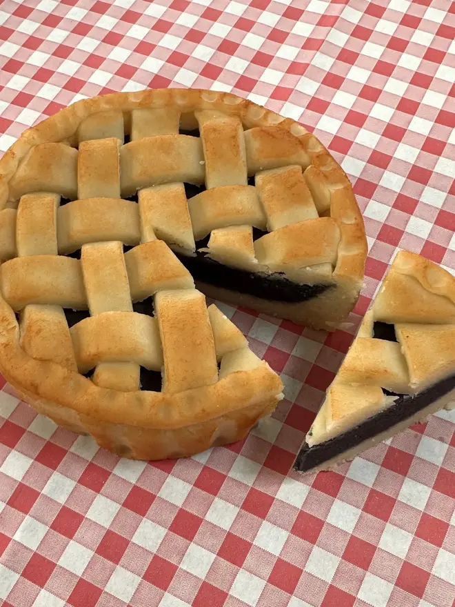 Marzipan Cherry Pie, marzipan cherry pie on a traditional picnic cloth. It has been cut and a slice rests next to the whole pie. 