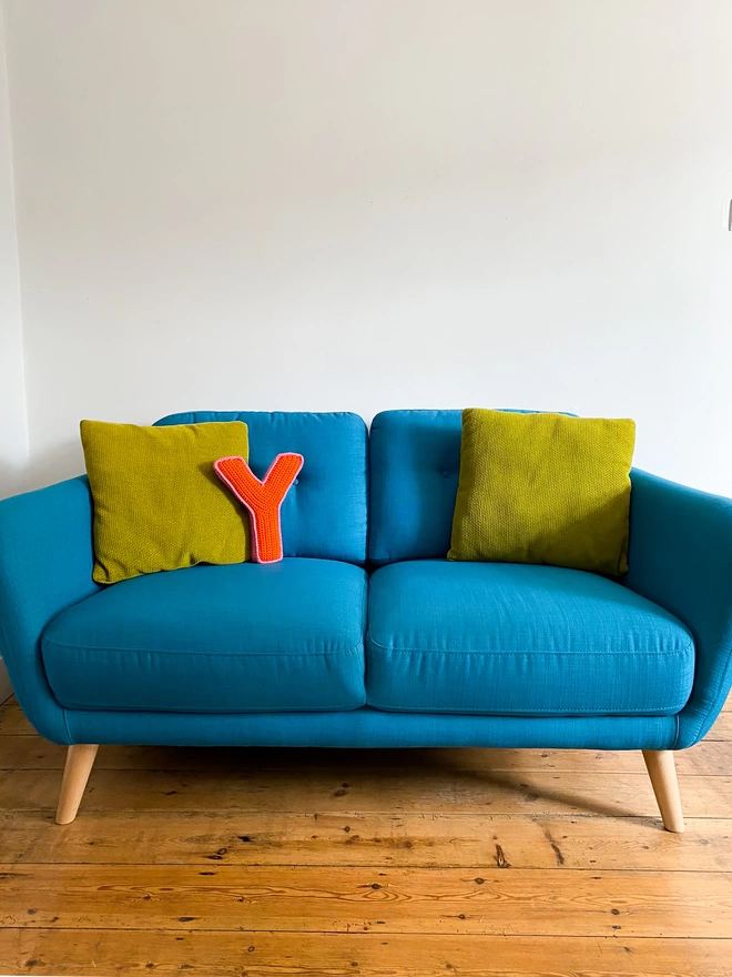 Crochet Y Cushion in Orange and Bubblegum Pink on a turquoise sofa