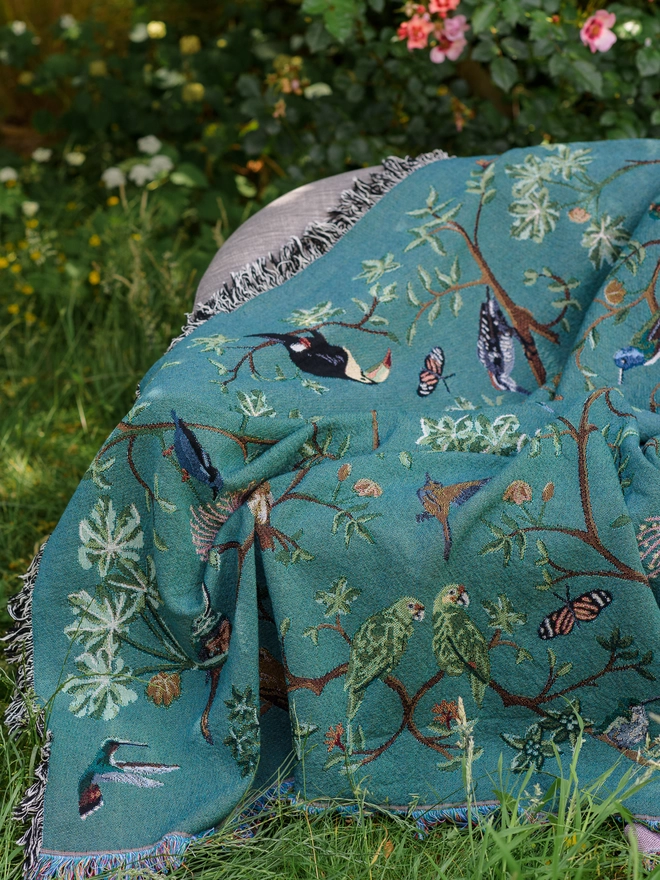 Forest Flight Blanket by Arcana seen on a sofa outside.