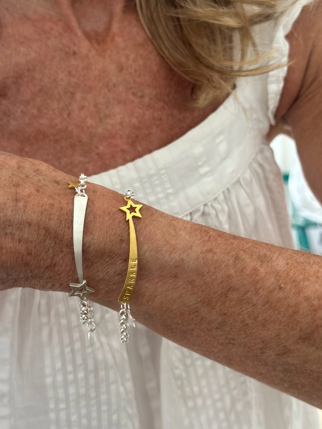 model wears a gold plate shooting star charm on a silver belcher chain bracelet, with small silver mini star, also wearing a sterling silver version