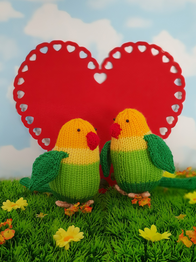 two knitted lovebirds with a big read heart behind them