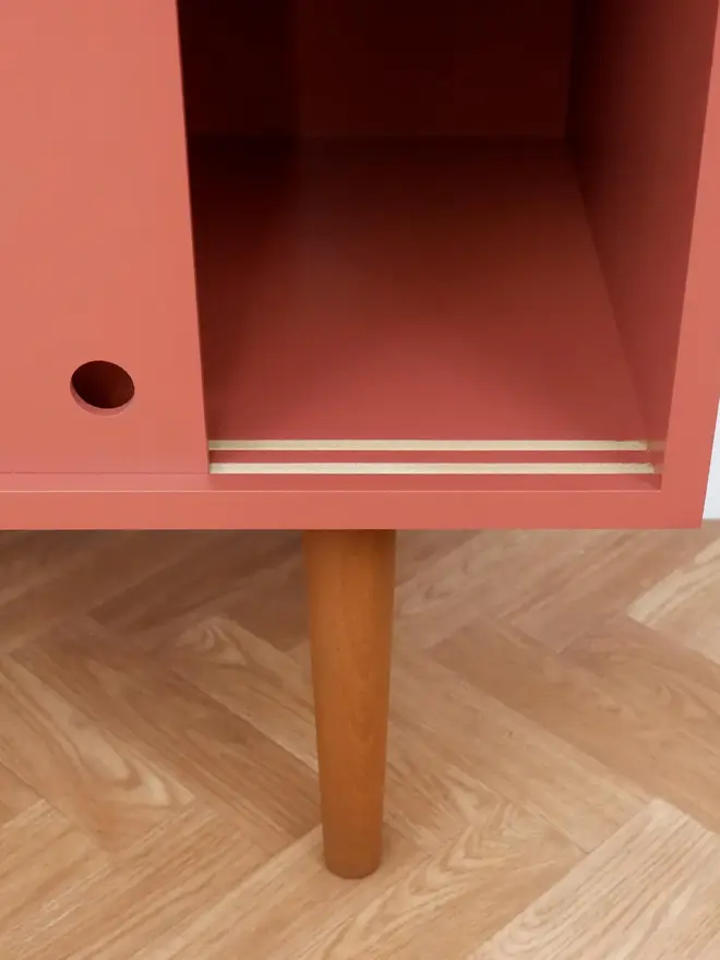 Mid-century cabinet with coral sliding doors and wooden tapered legs.