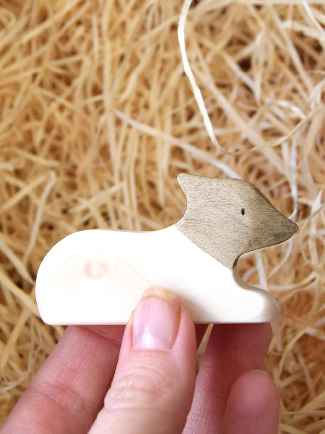 blacka nd white lamb lying down wooden toy held in hand above woodwool