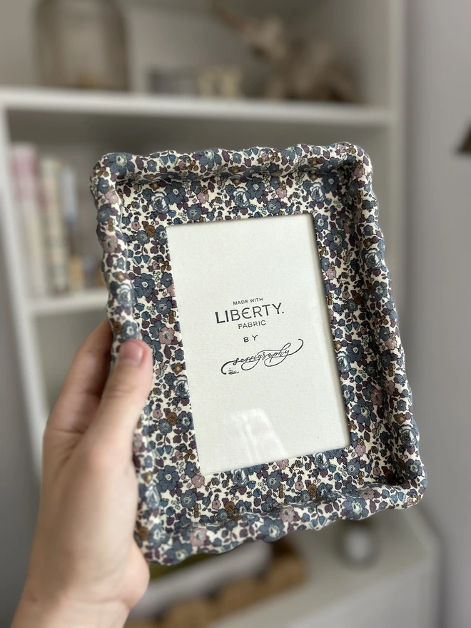 Liberty fabric covered wiggle mount frame held in hand against shelves