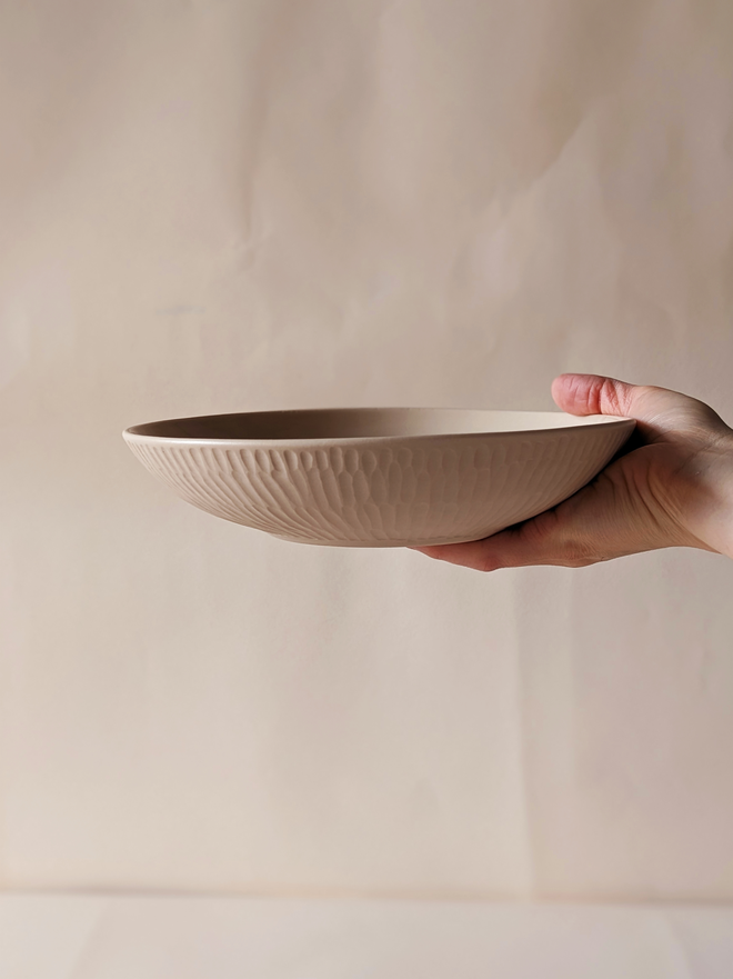 Porcelain Pasta Bowl in Pale Oat with hand carved scalloped details being held in a hand  