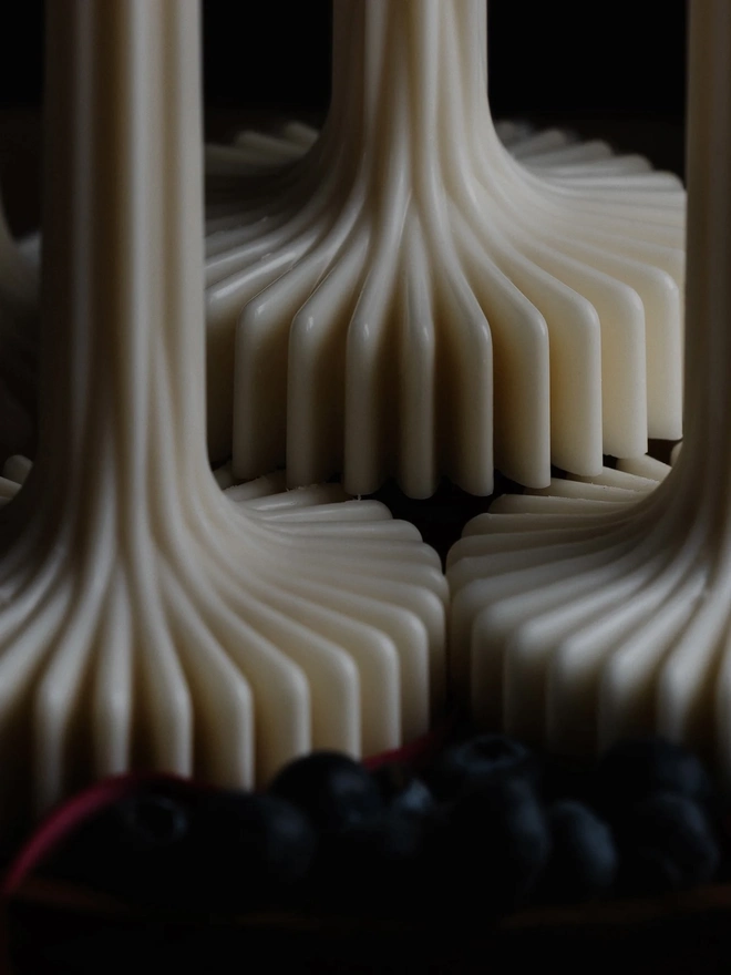 Pair Of White Flair Candles (Set Of 2). Close-up of the flared ribbed bases of cream sculptural candles, showing smooth vertical ridges that sweep outwards. The detail highlights the handcrafted precision behind each freestanding candle.
