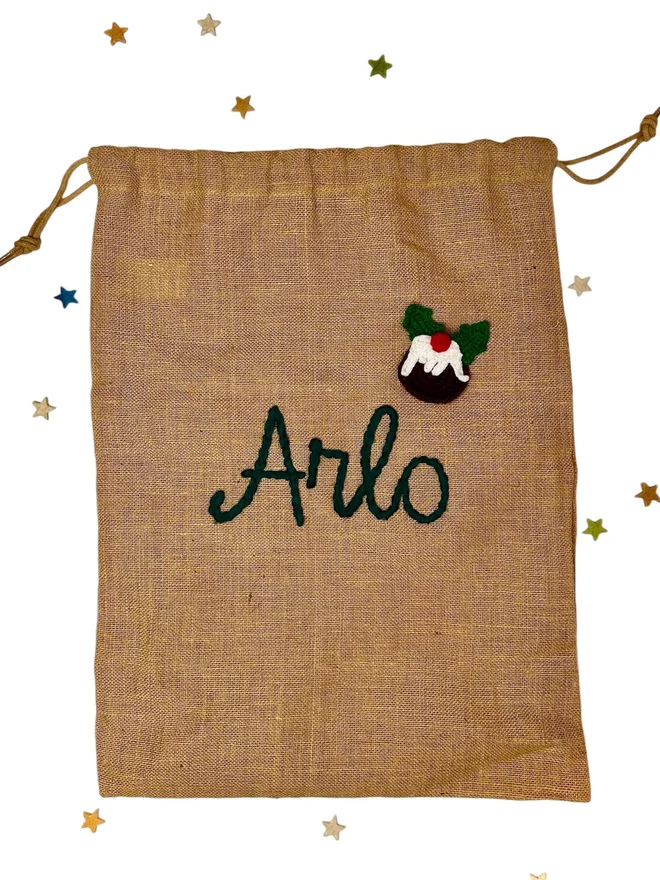 Personalised Christmas Sacks Arlo, a Christmas sack sitting on a white surface. It has its own personalisation, is surrounded by stars, and is accompanied by a Christmas pudding design. 