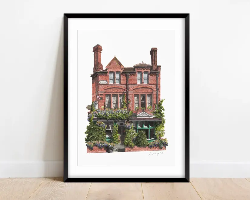 Nunhead Skehans Giclée Print (Unframed), a print of a brick pub in a black frame against a plain backdrop on a wooden surface. 