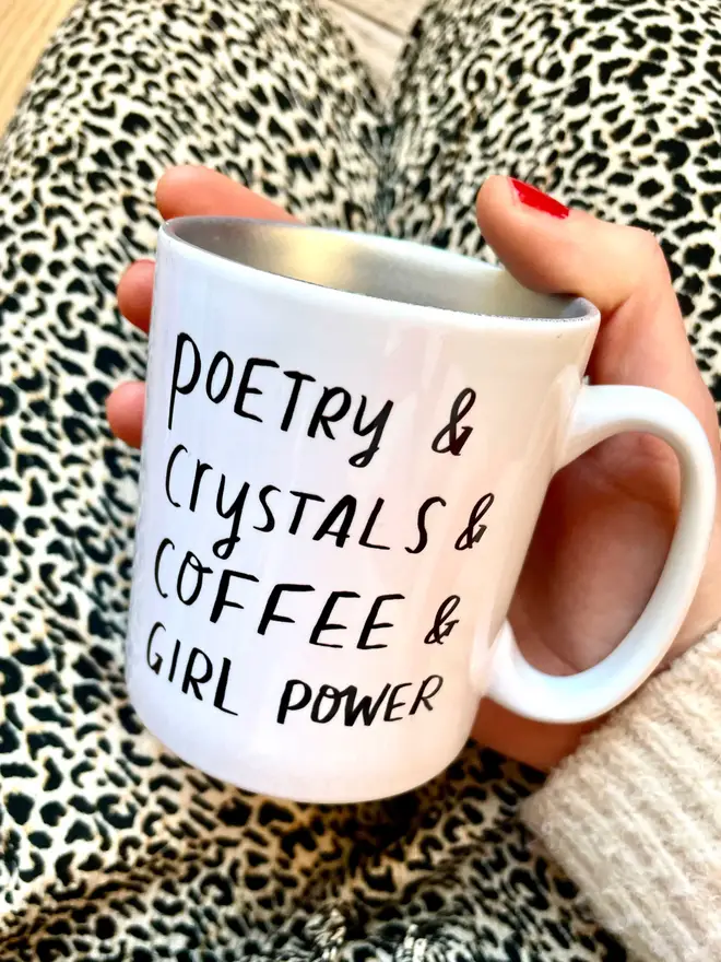 Holding mug which reads 'poetry & crystals & coffee & girl power' mug is silver inside