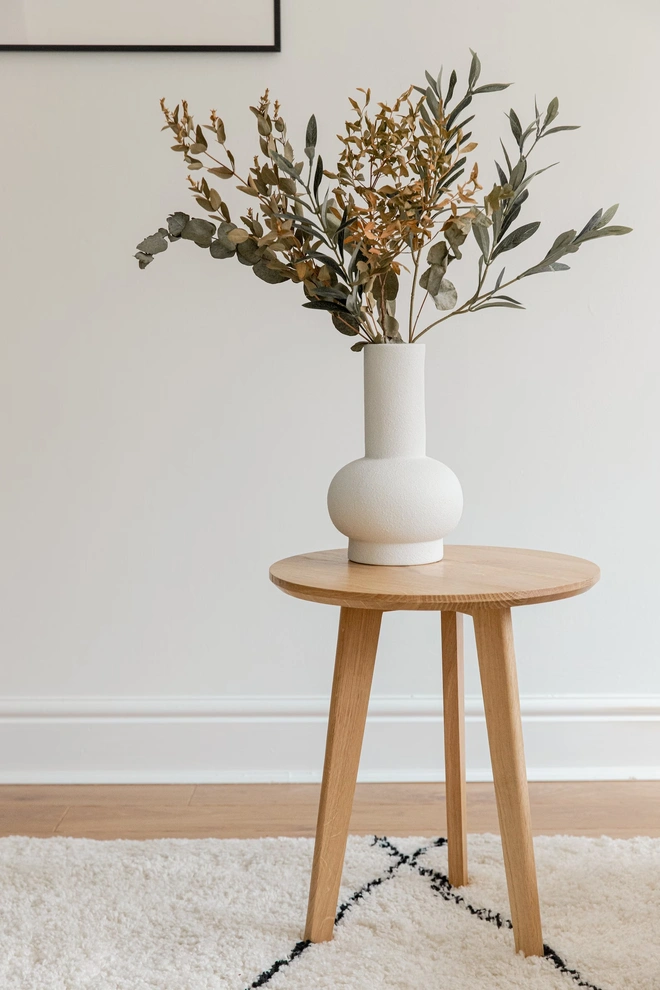 Handmade Solid Oak Side Table, a wooden side table sitting on a carpet in a living room. It is accompanied by a vase and a picture. 