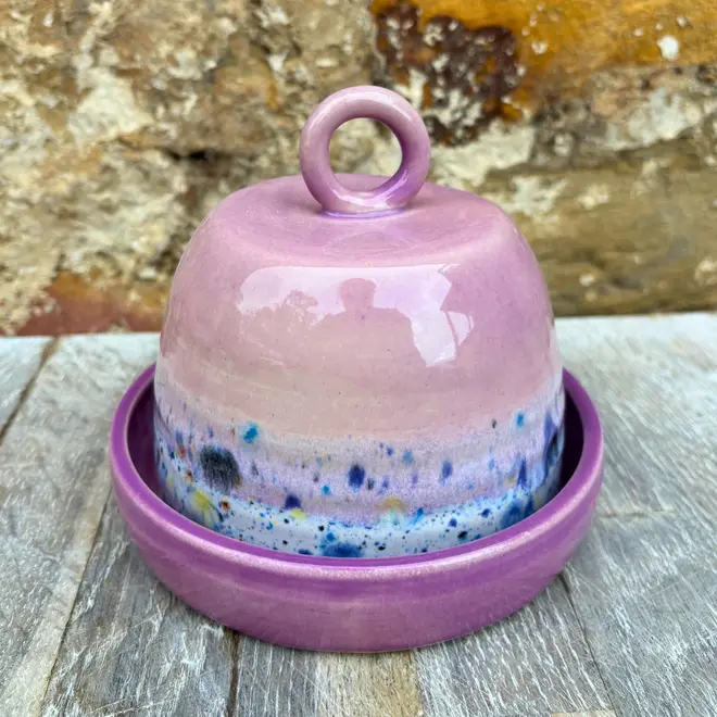 Shoreline Butter Dish, a colourful butter dish placed on a wooden surface against a brick wall. 