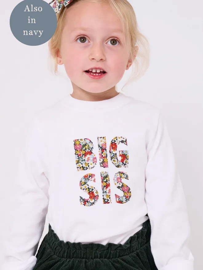 a little girl in a white t-shirt that says Big Sis in the front in floral print