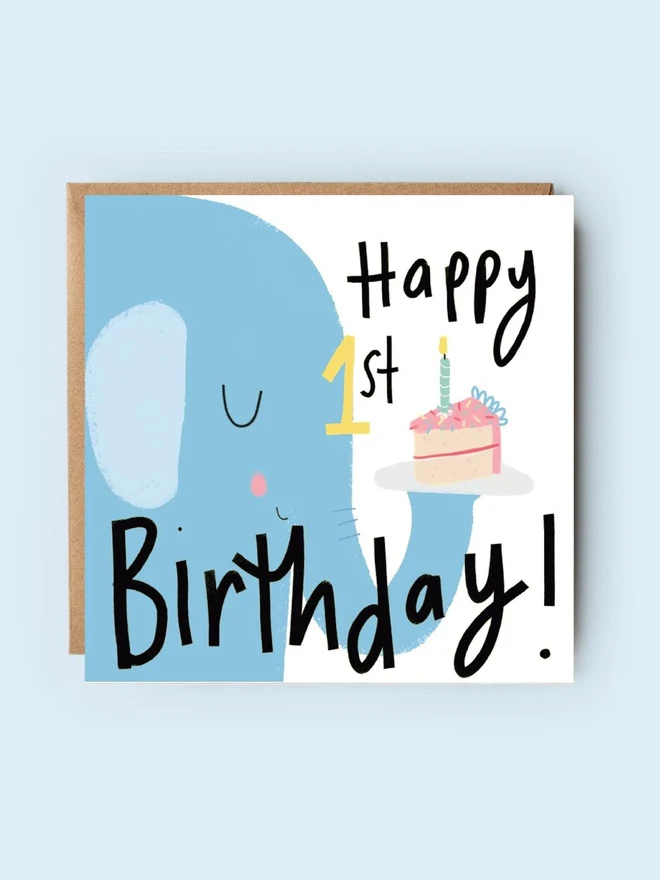 'happy 1st birthday' illustrated elephant card. card featuring a blue elephant holding a cake on its trunk. 