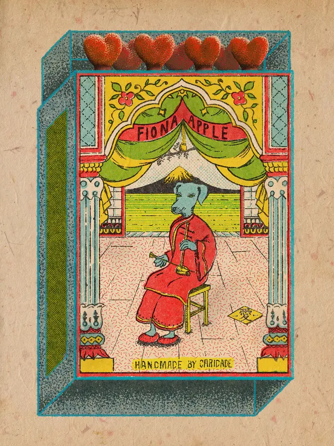 A surreal vintage-inspired matchbox illustration with the name “Fiona Apple” displayed on a red banner above a stage framed by ornate columns and green curtains. At center stage, a blue dog-headed figure dressed in a flowing red robe sits calmly on a wooden stool, holding a long smoking pipe. The tiled floor is patterned in pink, and the background opens to a stylized countryside landscape with striped green fields and a tiny thatched hut. Along the top edge of the box, five heart-shaped red match heads peek out, adding a playful touch. At the bottom, text reads: “Handmade by Caridade.” The overall effect is whimsical, theatrical, and dreamlike, blending animal fantasy with vintage ephemera.