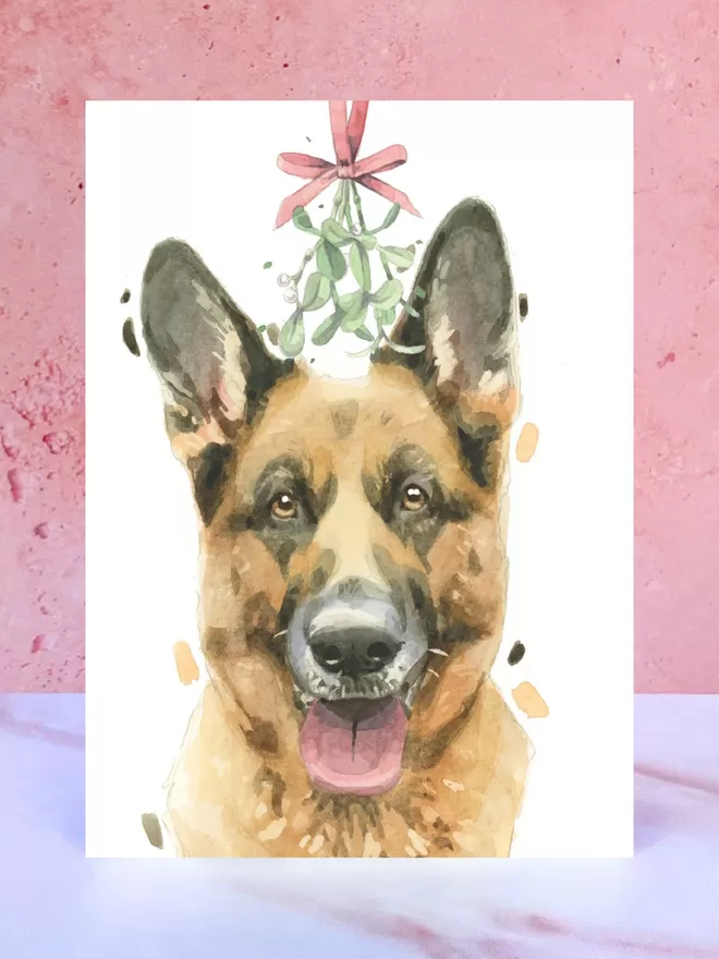 A Christmas card featuring a hand painted design of a German Shepherd, stood upright on a marble surface.