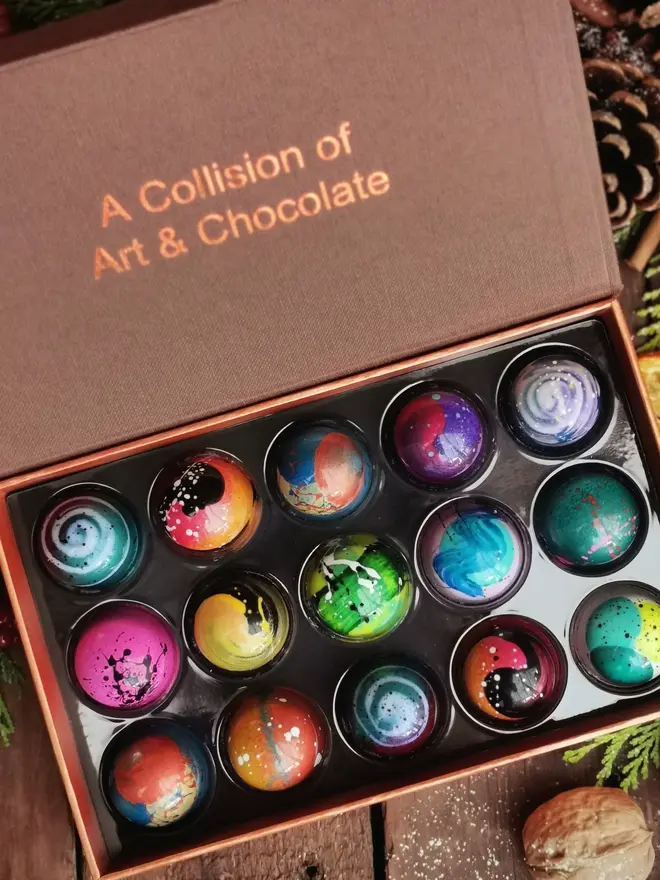 box of 15 beautifully decorated, colourful chocolates, on a background with pine cones and oranges