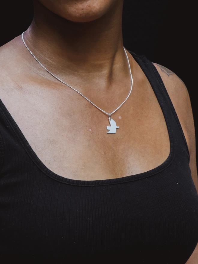 Woman wearing recycled sterling silver dove pendant necklace against black background