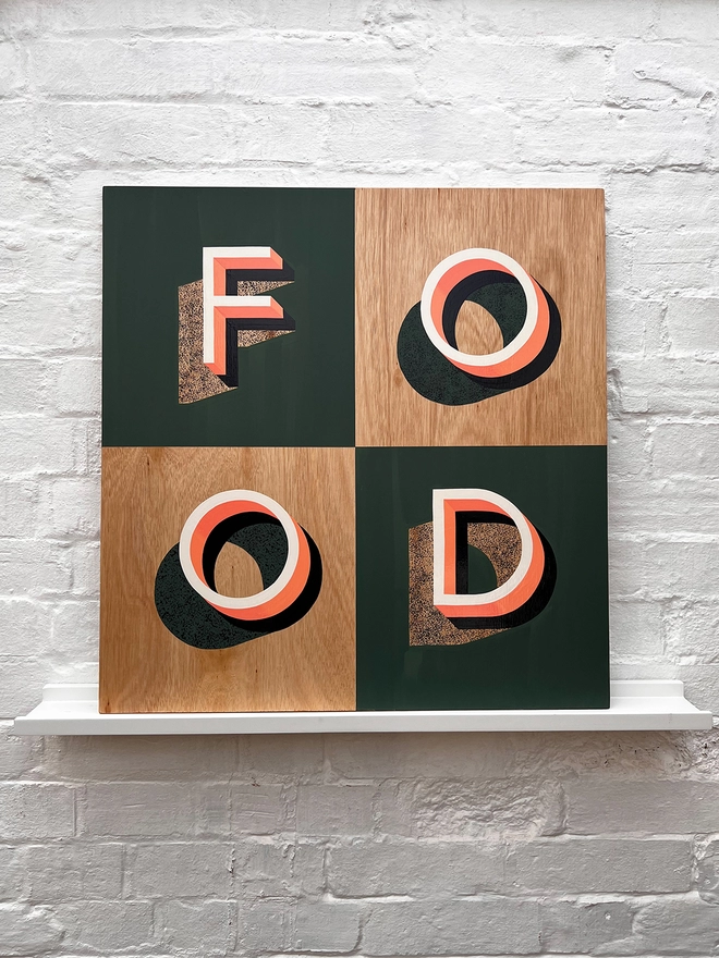 FOOD hand painted sign in coral, green and aubergine, against a white brick wall, straight on.