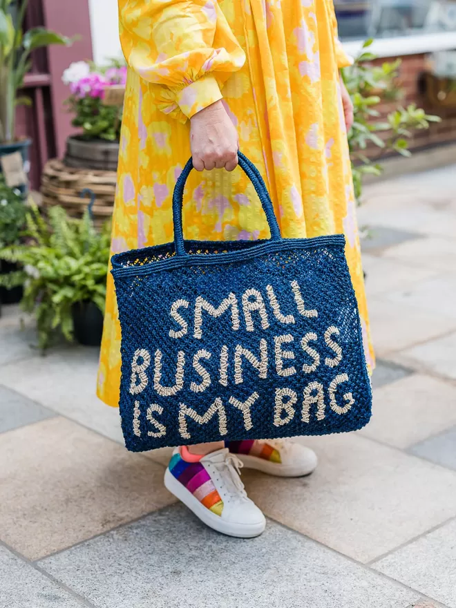 The Jacksons Small Business Is My Bag seen held by a woman in a yellow floral dress.