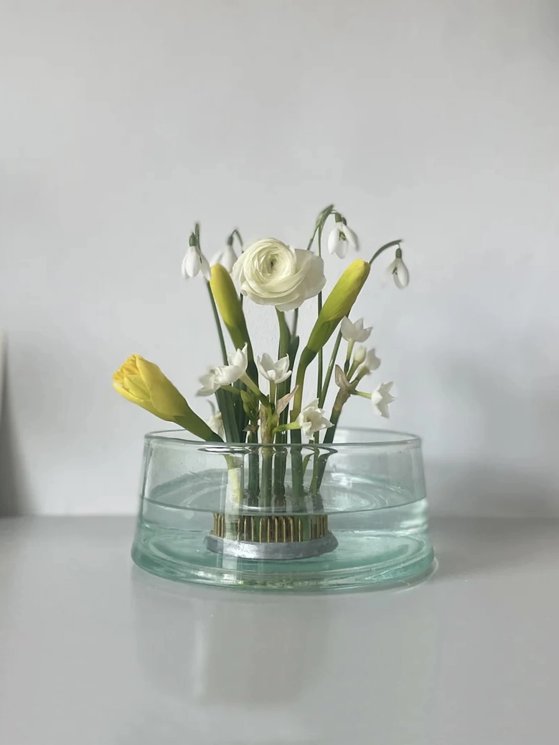 Extra Large Flower Arranging Items, a clear glass large flower vase sitting on a grey surface against a plain backdrop. It is filled by a group of flowers held together by a vase.  