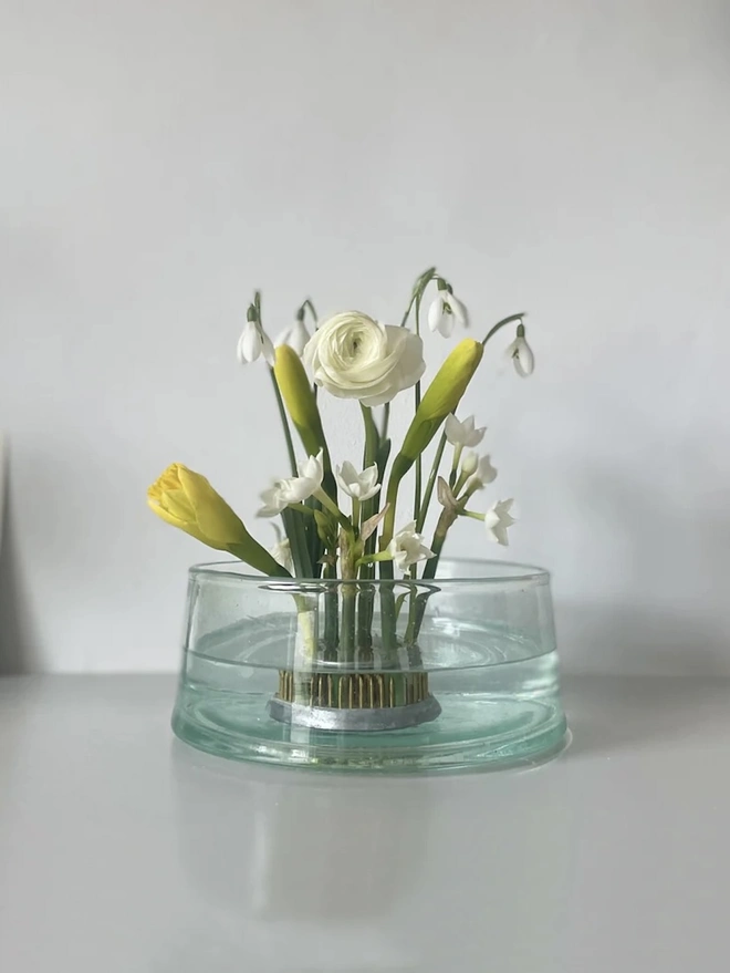 Extra Large Flower Arranging Items, a clear glass large flower vase sitting on a grey surface against a plain backdrop. It is filled by a group of flowers held together by a vase.  