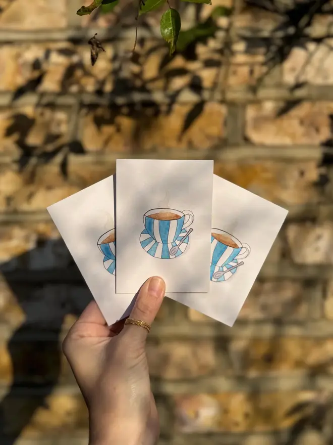cup and saucer illustrated mini cards (pack of 3). card set held against brick wall backdrop.