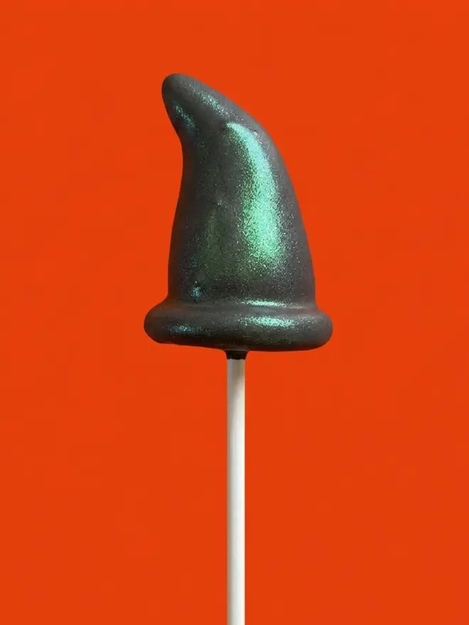 Black witches hat cake pop on a white stick against a bright orange background