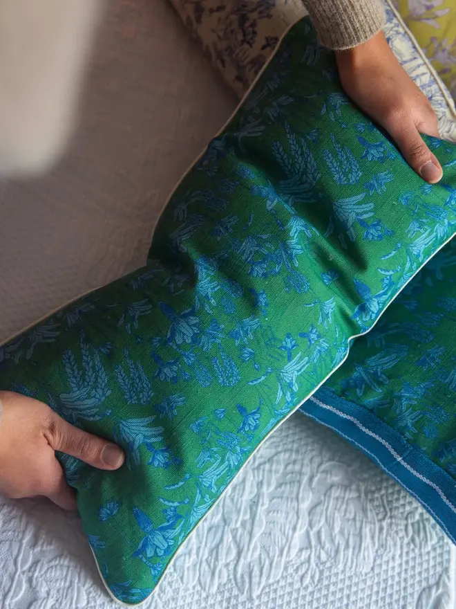 green tropicalia pattern cushion being held above a bed