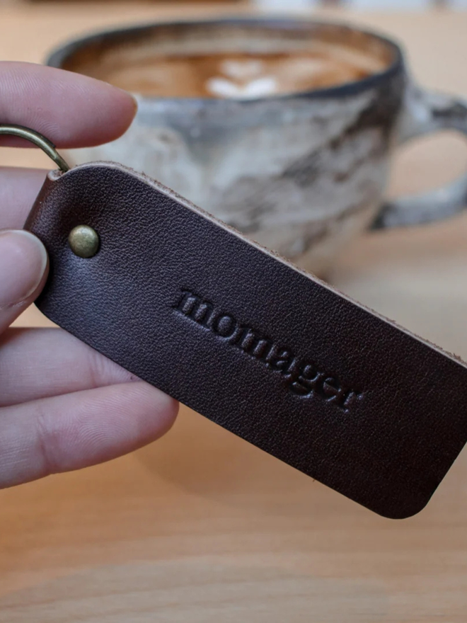 mother's day leather keyring. a hand holding a brown keyring embossed with 'momager'.