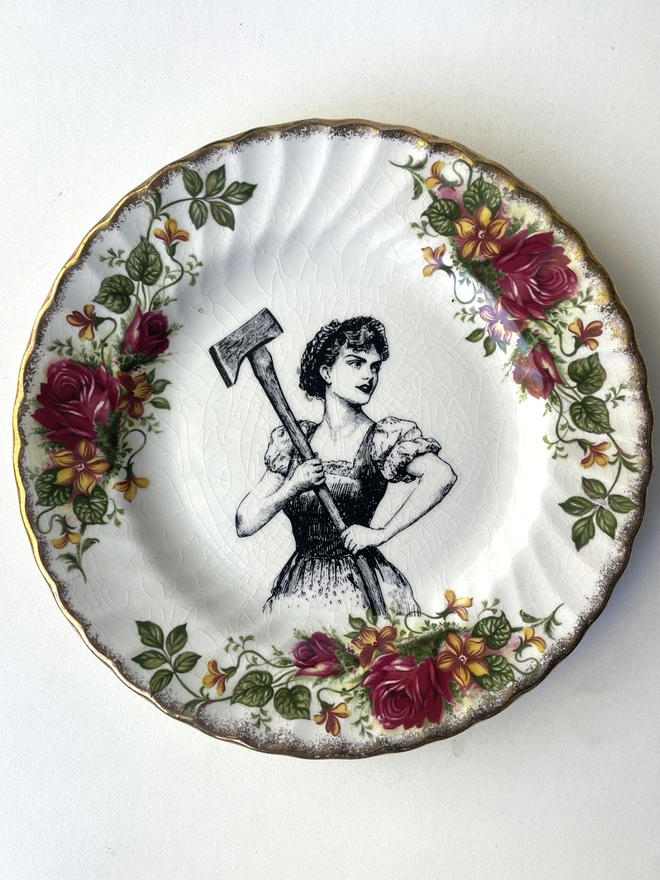 a vintage plate with a really ornate pretty border has a vintage black and white illustration of a beautiful girl in peasant clothes wielding an axe