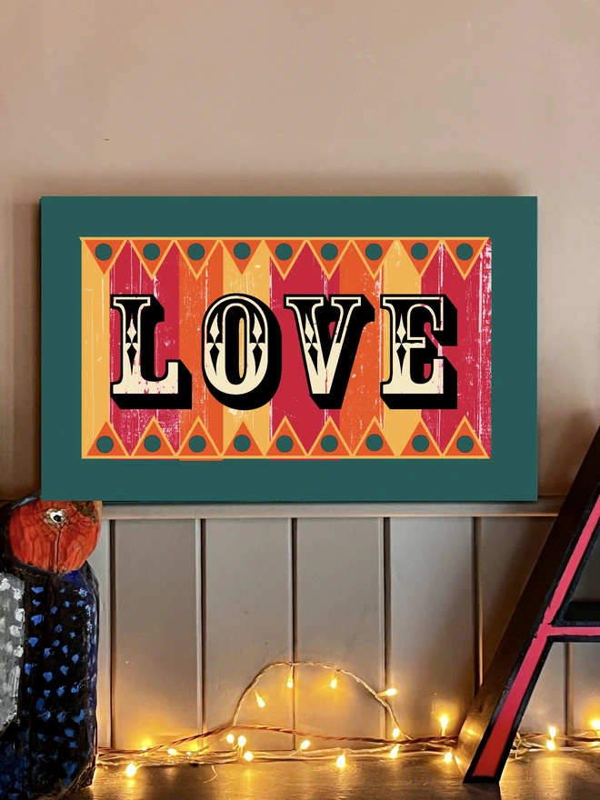 handpainted love sign in fairground lettering, with orange, pink and yello stripes and orange zig zags top and bottom surrounded by a teal frame