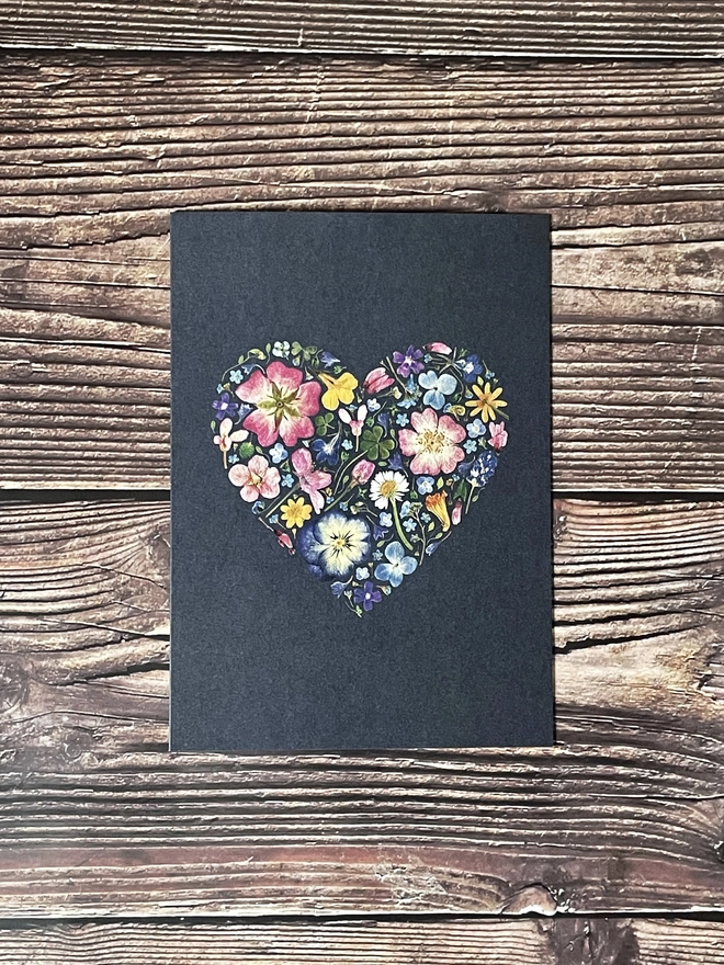 Dark Blue Greetings Card with Digitally Printed Pressed Flower Heart Design - Laying on Dark Brown Wooden Background
