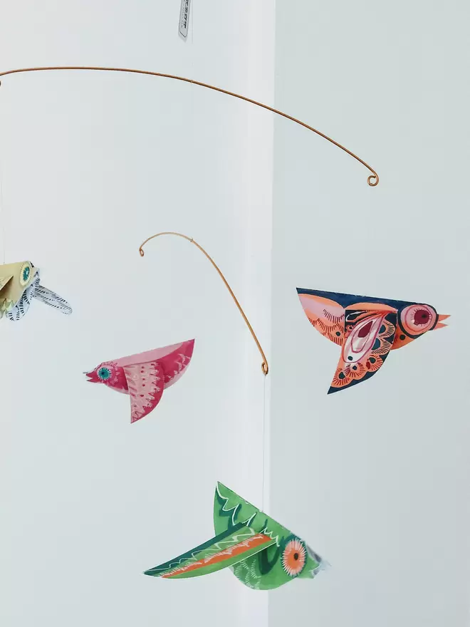 Colourful Paper Birds Mobile, with green, orange and pink patterned birds hanging against a white wall.  