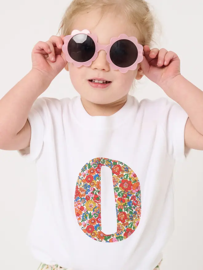 a 2 year old girl wearing a personalised kids white t-shirt with an initial cut from liberty floral print on the front