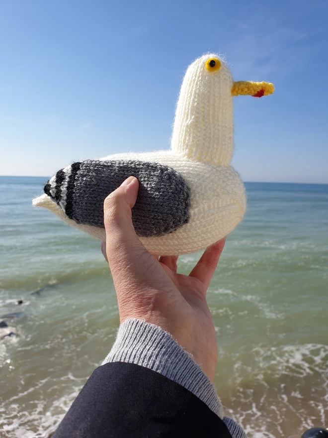 a knitted seagull being held up against a blue sky on a beach