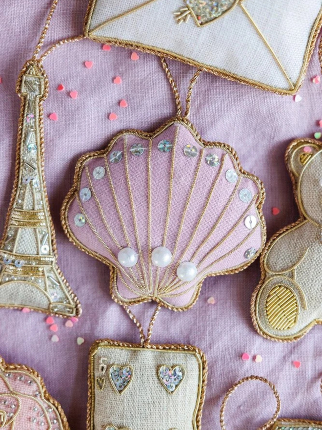 embroidered linen shell decoration. lilac shell decoration photographed against pink fabric background.