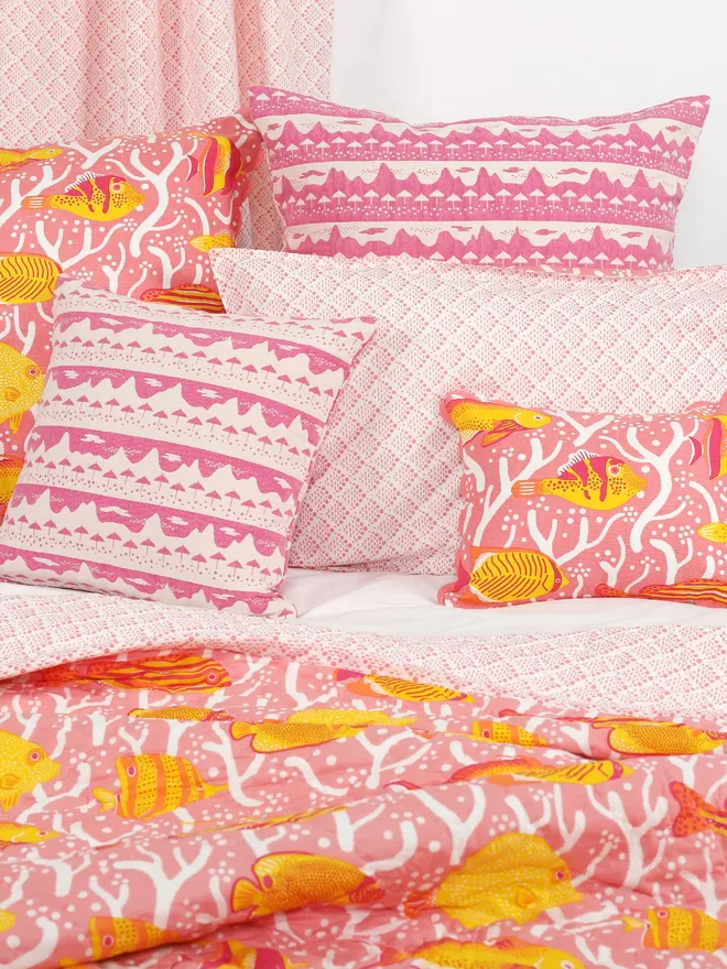 Pink Coral Reef Quilt, a pink quilt sitting on a bed. It is accompanied by some pillows. 