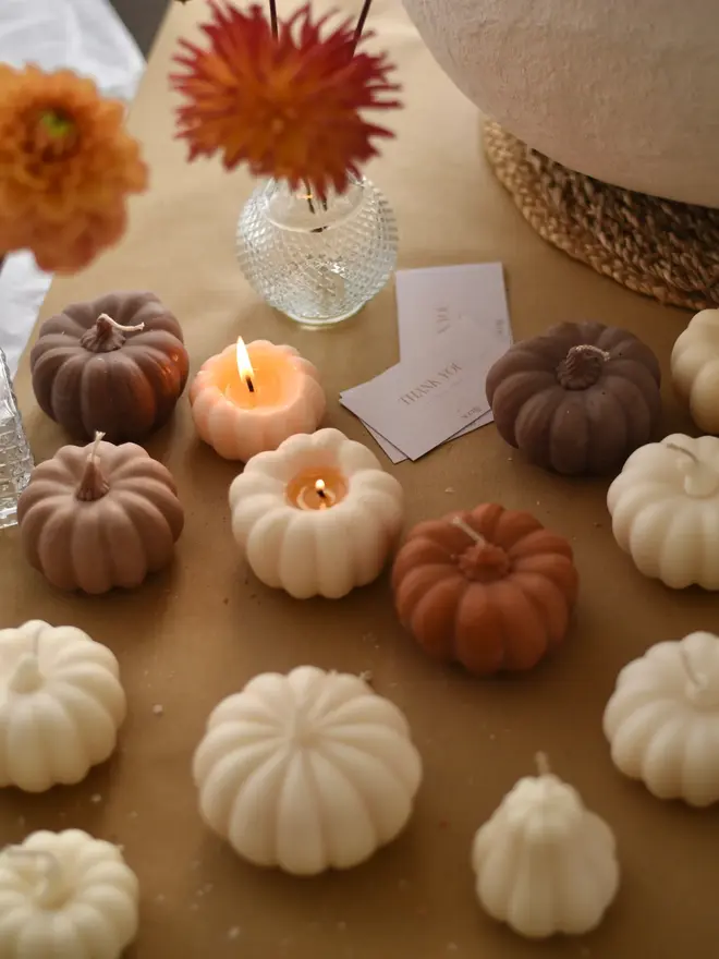 Medium Natural Wax Pumpkin Candle. An autumn table display of cream, terracotta and mocha pumpkin candles, two of them lit, styled with dahlias in glass vases and thank-you cards. The coordinating sculptural candles bring warmth and seasonal charm to any celebration.