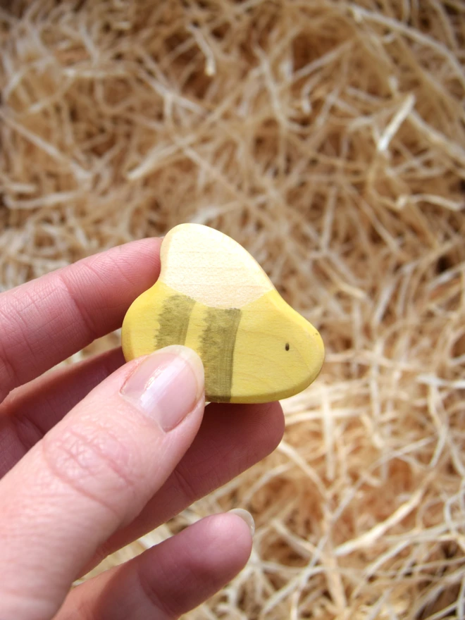 wooden toy bee being held above woodwool