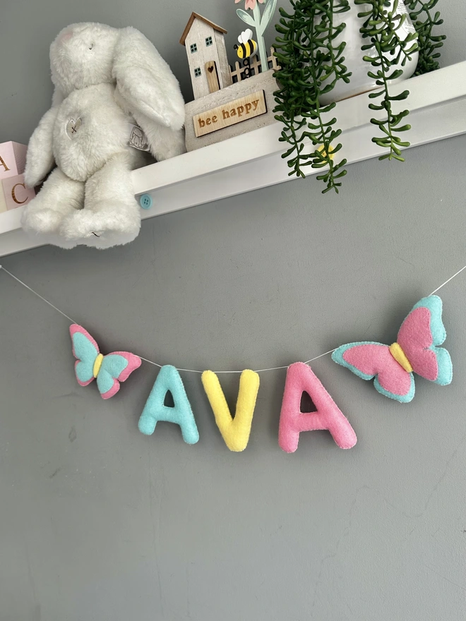 Personalised Name Icon Garland, a child’s name banner hanging from a white shelf, nursery decoration, baby gift