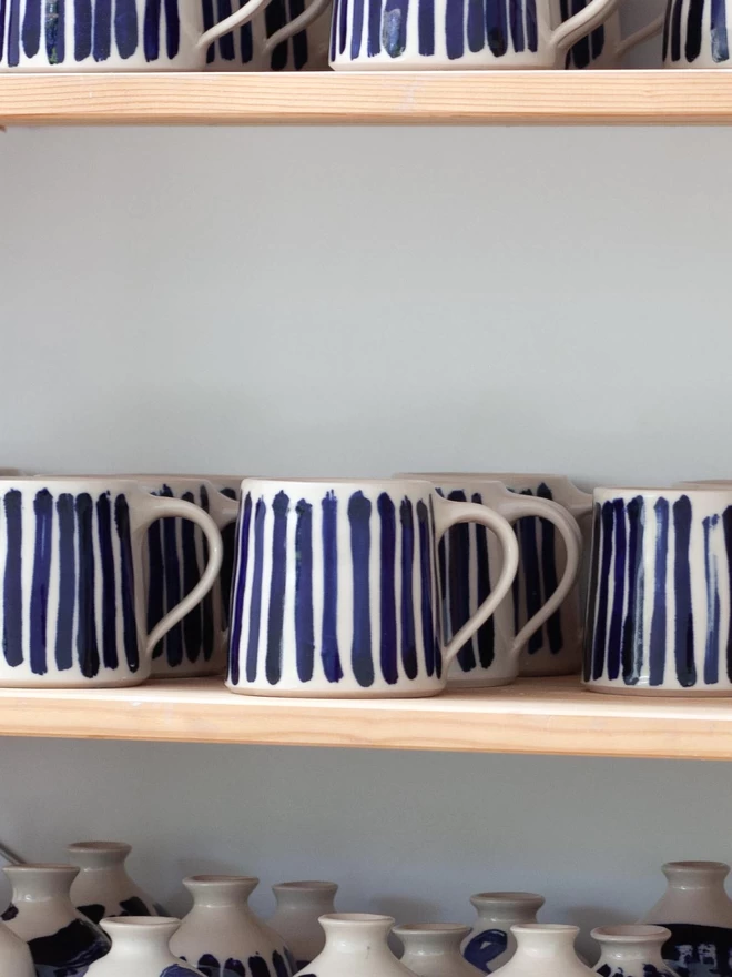 Gloss handmade mug with cobalt blue hand-painted stripes seen on shelves.