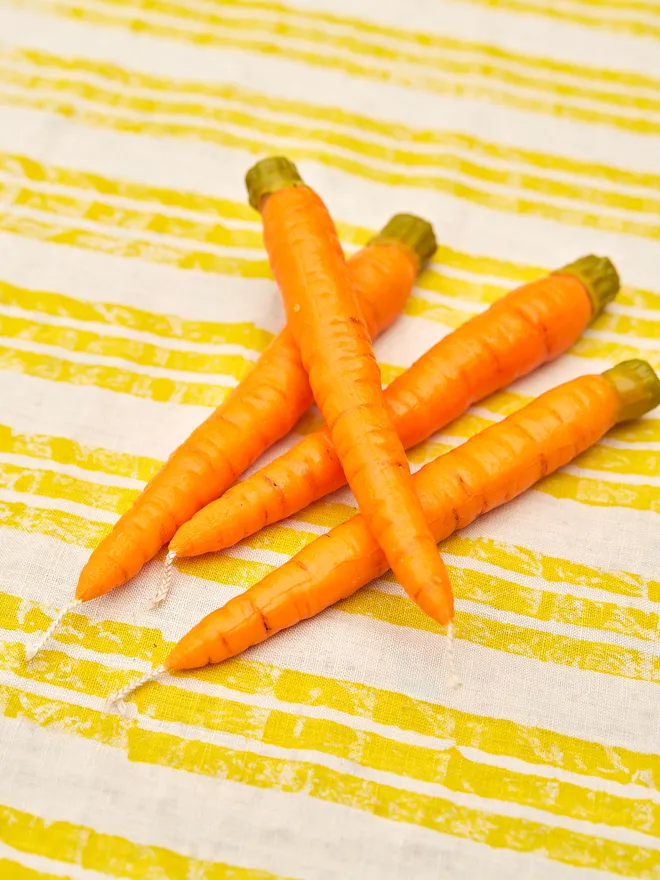 4 Fallow carrot dinner candles placed on a yellow and white stripped tablecloth 