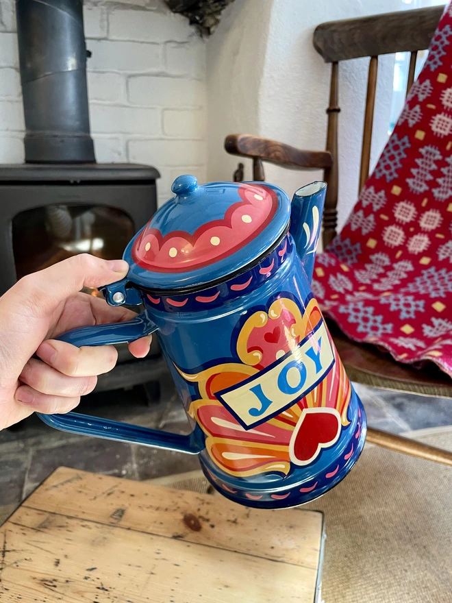 Blue vintage coffee pot, hand painted with a fairground inspired design in pink, orange and yellow. 'Joy' is painted in a banner through the centre of the design.