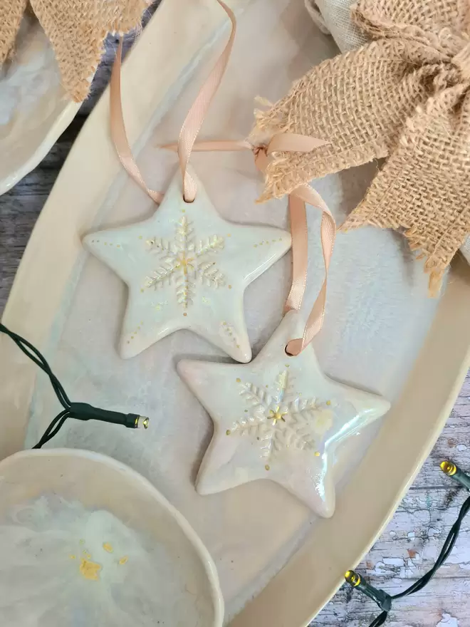 Star Christmas decorations, ceramic decorations, dream catcher, christmas star, pottery, Jenny Hopps Pottery, J.H Pottery, J.Hopps Pottery, Clay star, gift, christmas tree, pearlescent white and cream with gold details, on a light gold ribbon, photographed on a serving dish with Christmas lights