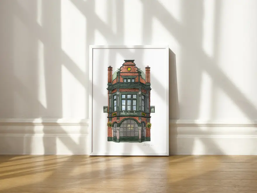 Borough The Roebuck Pub Giclée Print (Unframed), a print of a pub sitting in a white frame on a wooden surface against a plain backdrop.