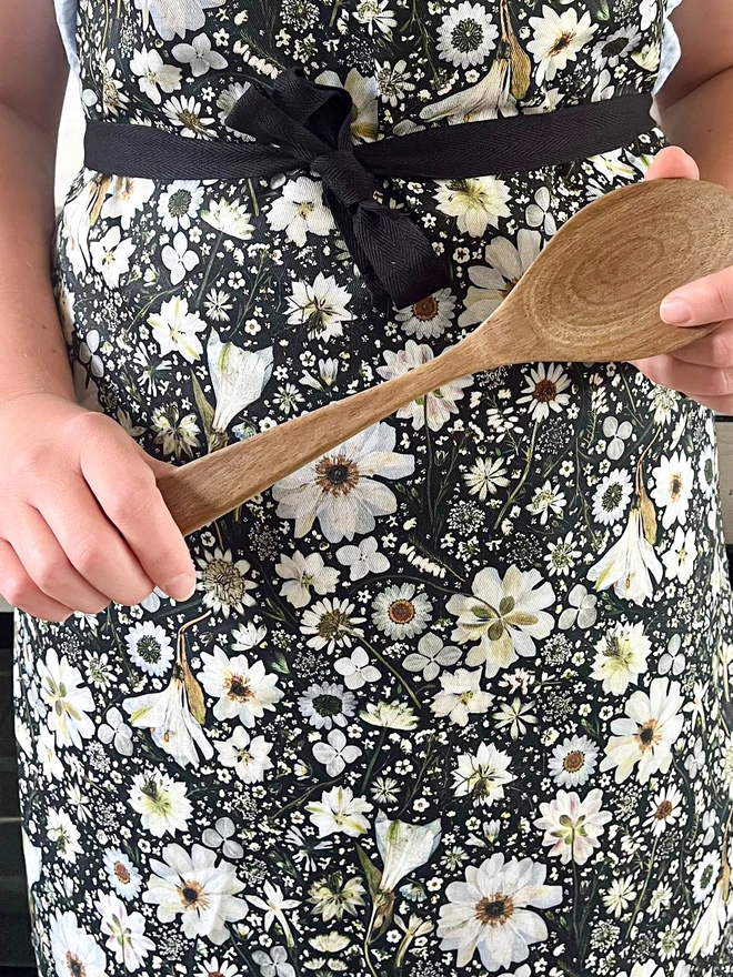 Nature-inspired apron with a floral design of white flowers on a black background. Flowers include Anemone, Nigella, Daisy, Astrantia, Heather, Hydrangea and Queen Anne’s Lace.