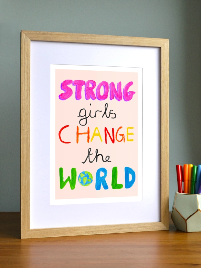 Art print saying 'Strong girls change the world' in a brown frame in a child's room