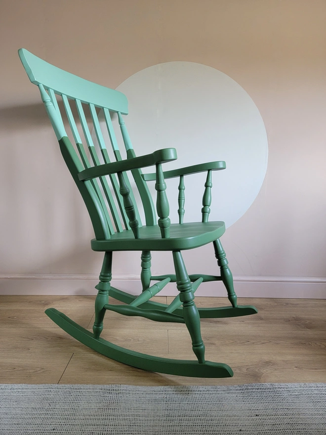 Green and mint painted wooden rocking chair with a pink wall background
