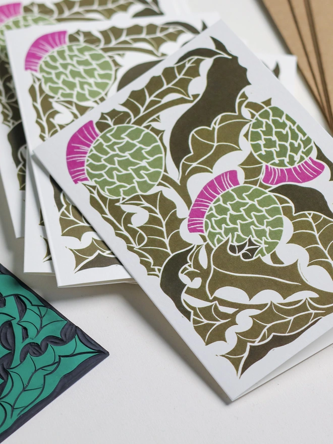 Set of 8 hand-carved botanical notecards featuring Scottish Thistles. A6 linocut print greeting cards in classic thistle green, displayed with kraft envelopes. Cottagecore stationery on recycled cardstock.