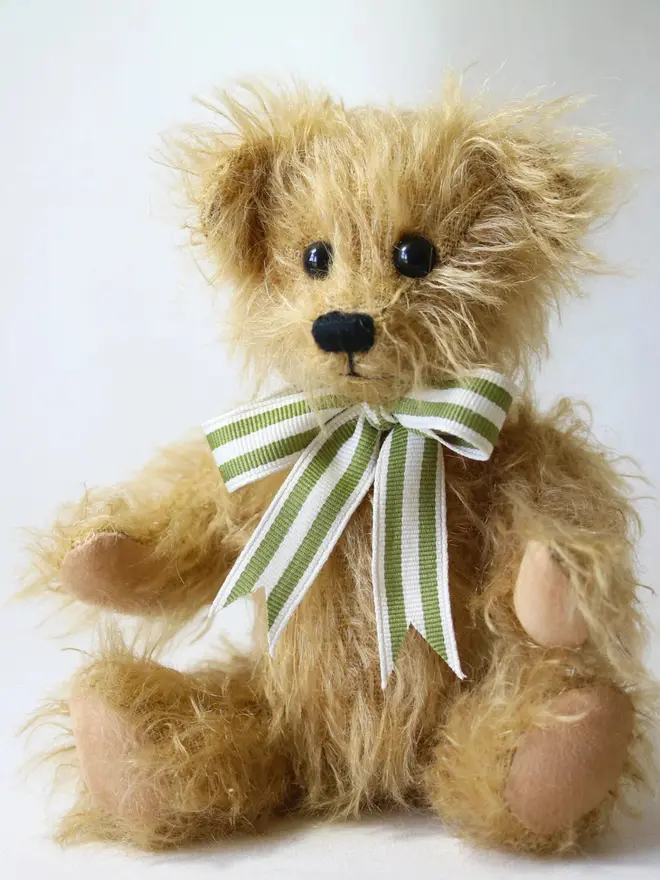 Handmade brown teddy bear sitting upright with a green striped ribbon bow against a plain background.